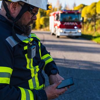 Fireman looking at his smartphone displaying Agnet user interface next to a fire truck and forest
