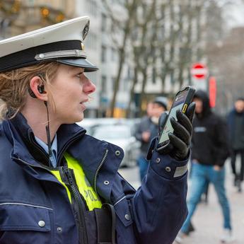 Police woman using Agnet group call feature on a ruggedized smartphone in the street