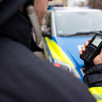 public_safety_worker_holding_tetra_device_police_car_in_the_back