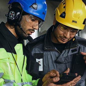 Two helmeted industry workers looking at smart device