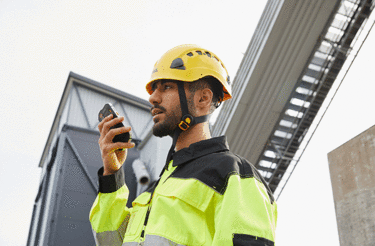 entreprises business critical industry user with a yellow helmet speaking to a smartphone entreprises business critical industry user with a yellow helmet speaking to a smartphone