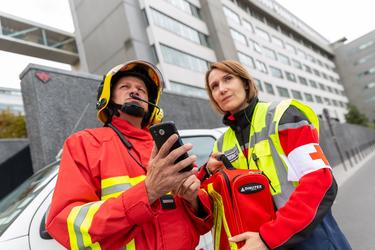 Fireman holding smartphone and paramedic woman holding medipack looking offscreen Fireman holding smartphone and paramedic woman holding medipack looking offscreen