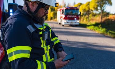 Fireman looking at his smartphone displaying Agnet user interface next to a fire truck and forest Fireman looking at his smartphone displaying Agnet user interface next to a fire truck and forest