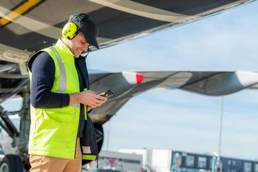 Maintenance guy on the tarmac using his ruggedized smartphone for an aircraft turnaround Maintenance guy on the tarmac using his ruggedized smartphone for an aircraft turnaround