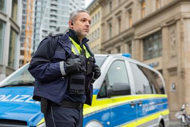 Policeman equipped with ruggedized smartphone and PTT accessory watching in the street next to a police car Policeman equipped with ruggedized smartphone and PTT accessory watching in the street next to a police car