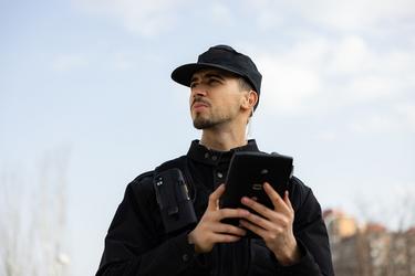 Security guy equipped with ruggedized smartphone and tablet watching in the city Security guy equipped with ruggedized smartphone and tablet watching in the city