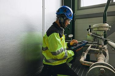 Worker with smart device next to factory equipment Worker with smart device next to factory equipment