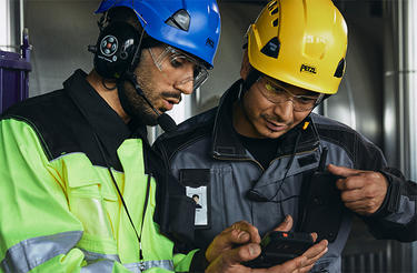 Two helmeted industry workers looking at smart device