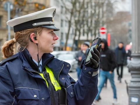 Police woman using Agnet group call feature on a ruggedized smartphone in the street