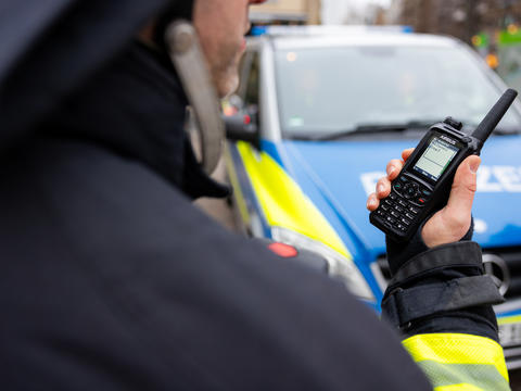 public_safety_worker_holding_tetra_device_police_car_in_the_back