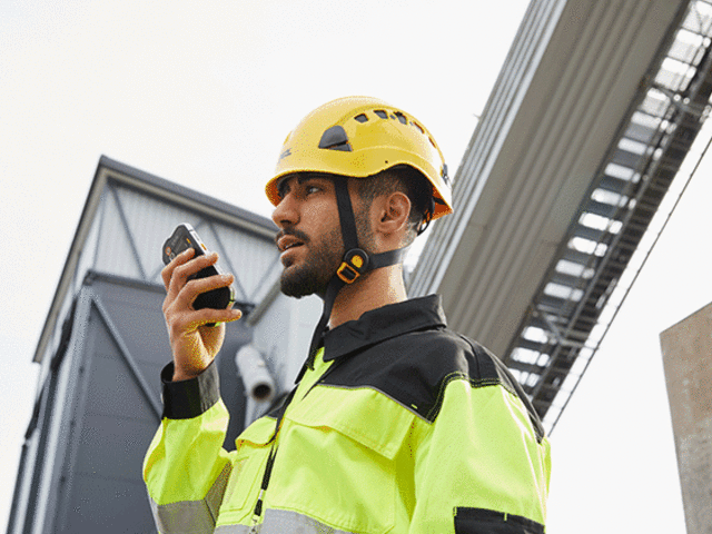 entreprises business critical industry user with a yellow helmet speaking to a smartphone 