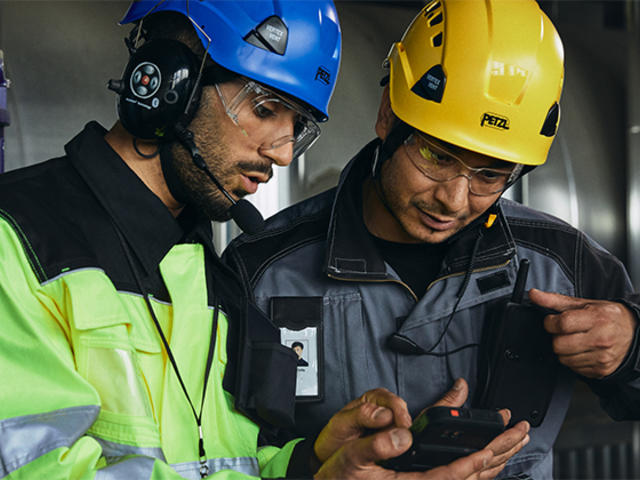 Two helmeted industry workers looking at smart device