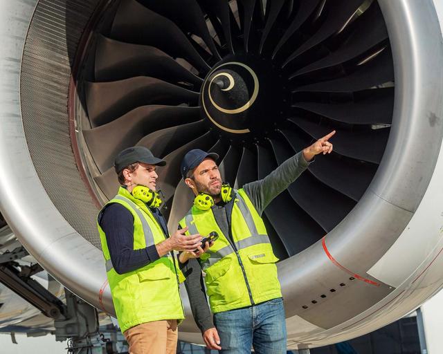 Ground handlers discussing in front of a airplane jet engine