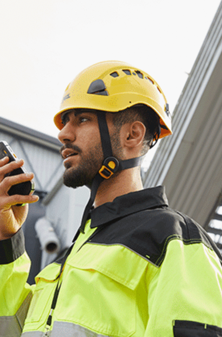 entreprises business critical industry user with a yellow helmet speaking to a smartphone 
