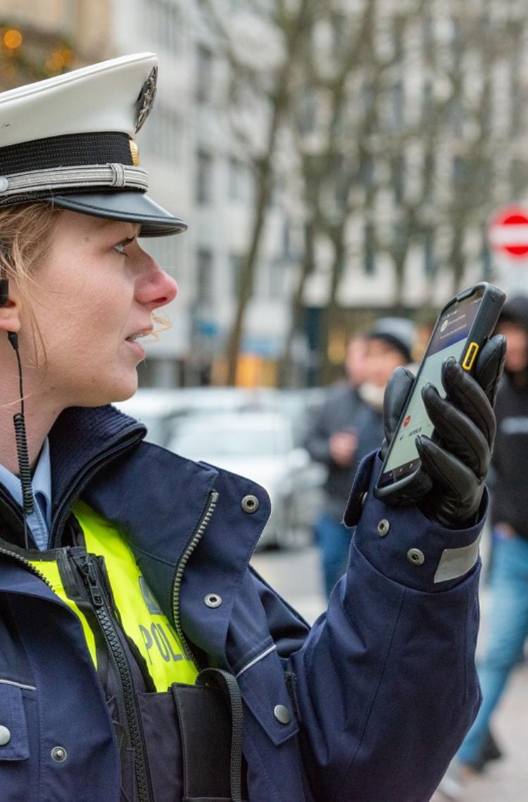 Police woman using Agnet group call feature on a ruggedized smartphone in the street Police woman using Agnet group call feature on a ruggedized smartphone in the street