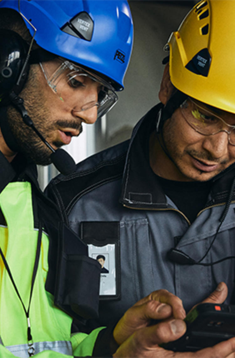 Two helmeted industry workers looking at smart device